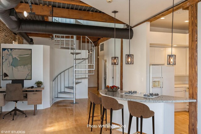 kitchen with light wood-type flooring, a kitchen bar, light stone counters, decorative light fixtures, and white appliances