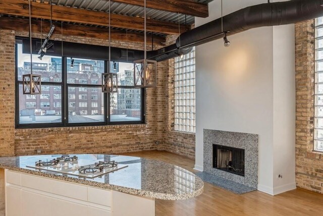 unfurnished living room with beam ceiling, plenty of natural light, light hardwood / wood-style floors, and brick wall