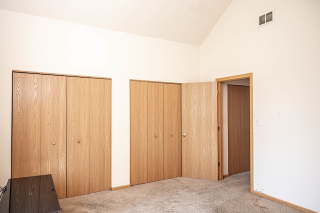 unfurnished bedroom with light colored carpet, two closets, and high vaulted ceiling