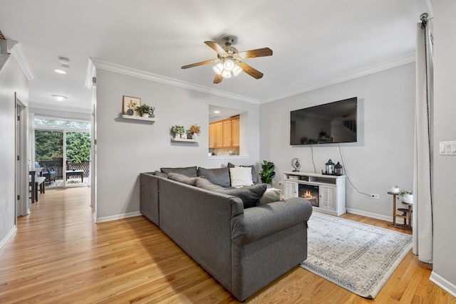 living area with light wood-style flooring, ornamental molding, baseboards, and a glass covered fireplace