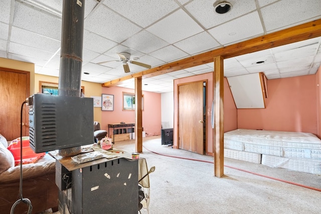 bedroom featuring ceiling fan, a drop ceiling, a wood stove, and carpet flooring