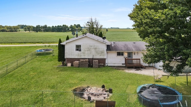 rear view of property featuring a rural view, a yard, a trampoline, and a deck