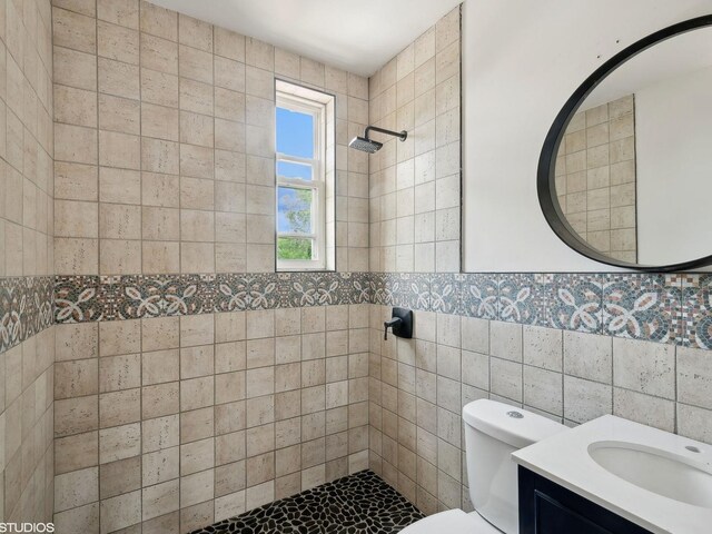 bathroom featuring toilet, tiled shower, tile walls, and vanity