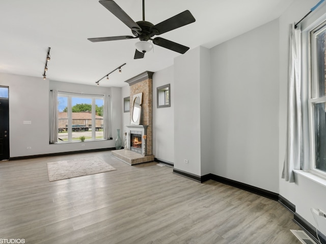 unfurnished living room featuring brick wall, a fireplace, light hardwood / wood-style floors, ceiling fan, and track lighting