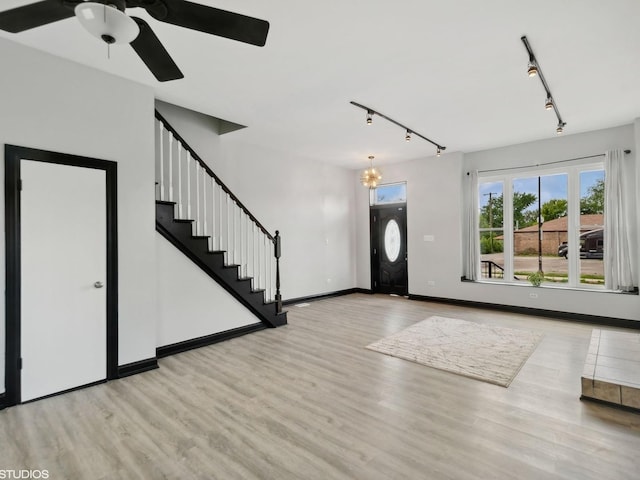foyer entrance with stairway, wood finished floors, rail lighting, baseboards, and ceiling fan with notable chandelier