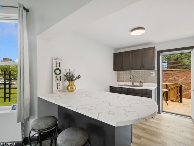 kitchen with tasteful backsplash, a breakfast bar area, light wood-type flooring, a sink, and a peninsula