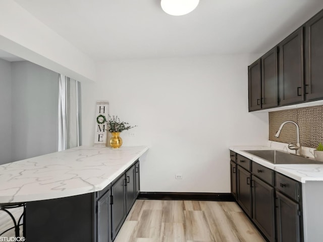 kitchen featuring decorative backsplash, a sink, light stone counters, light wood finished floors, and a peninsula