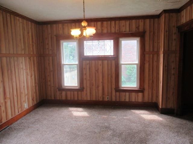 unfurnished dining area featuring a notable chandelier, crown molding, carpet floors, and wooden walls