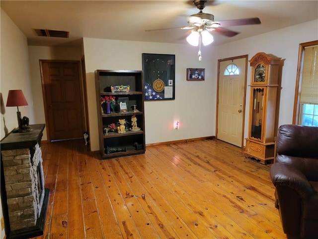 sitting room featuring a stone fireplace, hardwood / wood-style floors, and ceiling fan