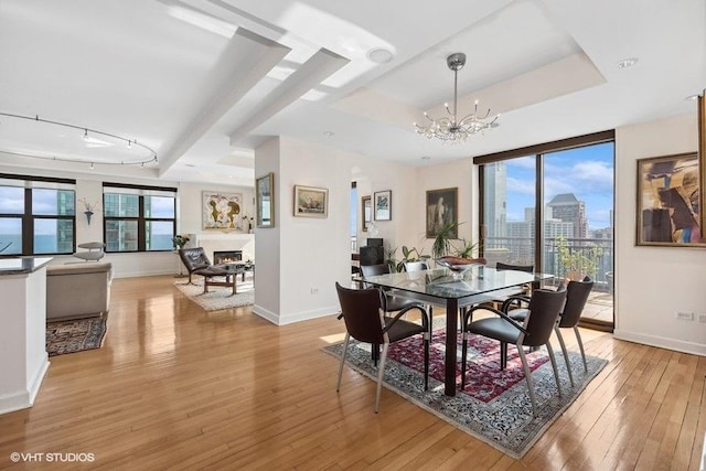 dining space with a notable chandelier, light hardwood / wood-style flooring, a raised ceiling, and plenty of natural light