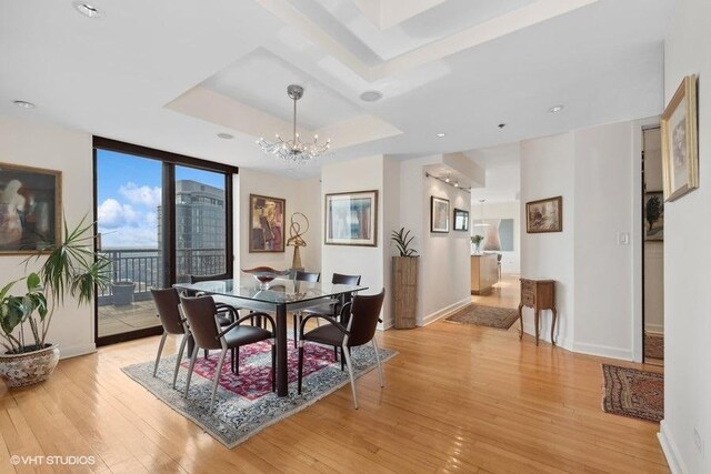 dining space featuring an inviting chandelier, a raised ceiling, expansive windows, and light wood-type flooring