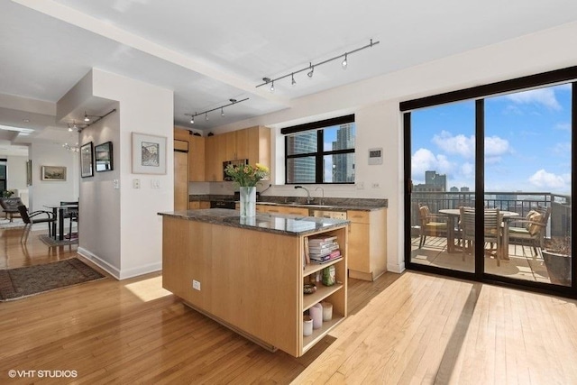 kitchen with dark stone countertops, a center island, sink, and light wood-type flooring