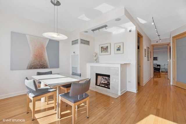 dining space with a high end fireplace, rail lighting, and light wood-type flooring