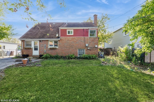 rear view of house with a yard, brick siding, a chimney, and fence