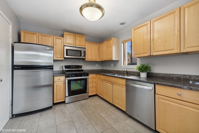 kitchen featuring light brown cabinets, sink, light tile patterned flooring, dark stone counters, and appliances with stainless steel finishes