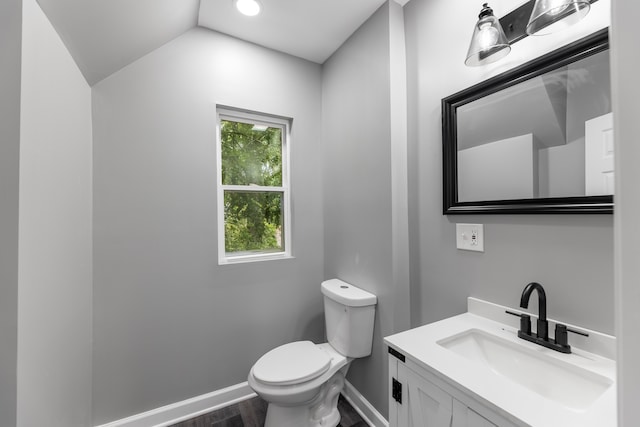 bathroom with hardwood / wood-style floors, vaulted ceiling, toilet, and vanity