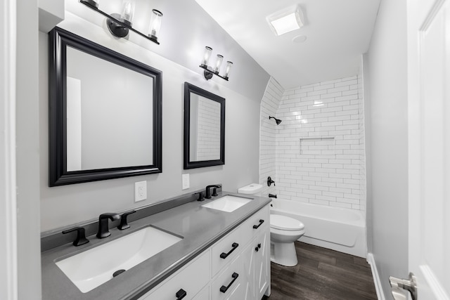 full bathroom featuring toilet, tiled shower / bath, dual bowl vanity, and wood-type flooring