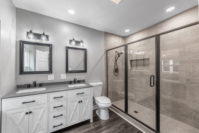 bathroom with a shower with shower door, toilet, dual bowl vanity, and wood-type flooring