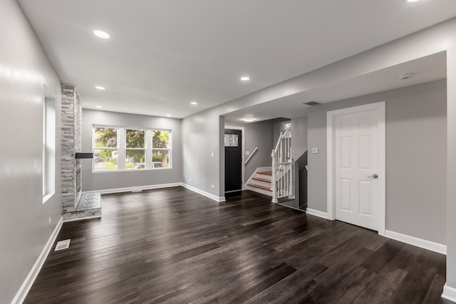 unfurnished living room with a stone fireplace and dark wood-type flooring