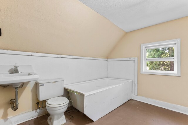 bathroom with vaulted ceiling, a textured ceiling, toilet, and a washtub