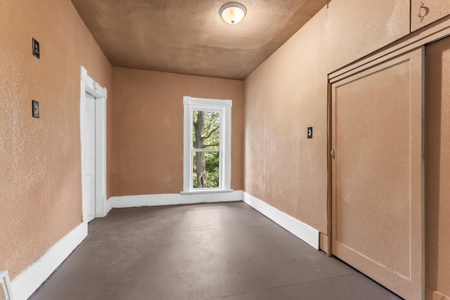 empty room featuring a textured ceiling, concrete flooring, a textured wall, and baseboards
