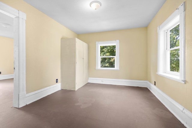 empty room with a wealth of natural light, concrete floors, and baseboards