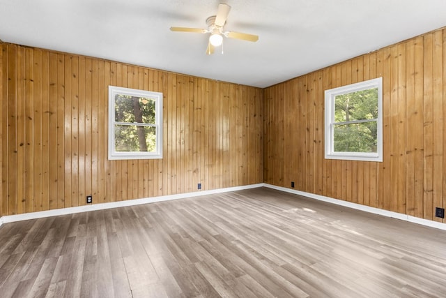 empty room featuring ceiling fan, baseboards, wood finished floors, and a healthy amount of sunlight