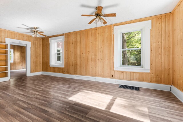 empty room with ceiling fan, wood walls, and wood-type flooring