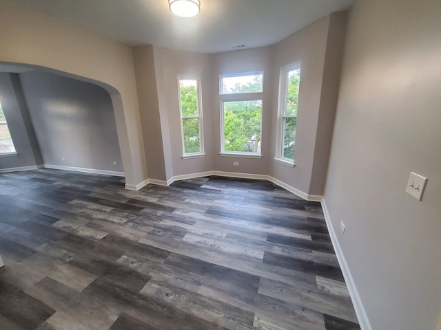 empty room featuring arched walkways, dark wood finished floors, and baseboards