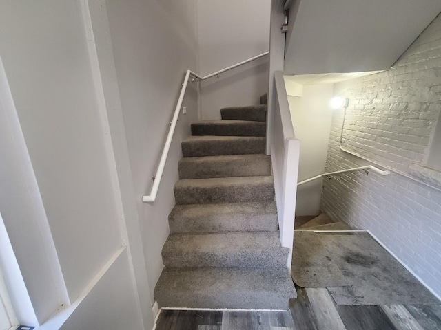 stairs featuring wood finished floors and brick wall