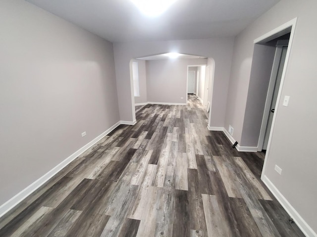 corridor featuring dark wood finished floors, baseboards, and arched walkways