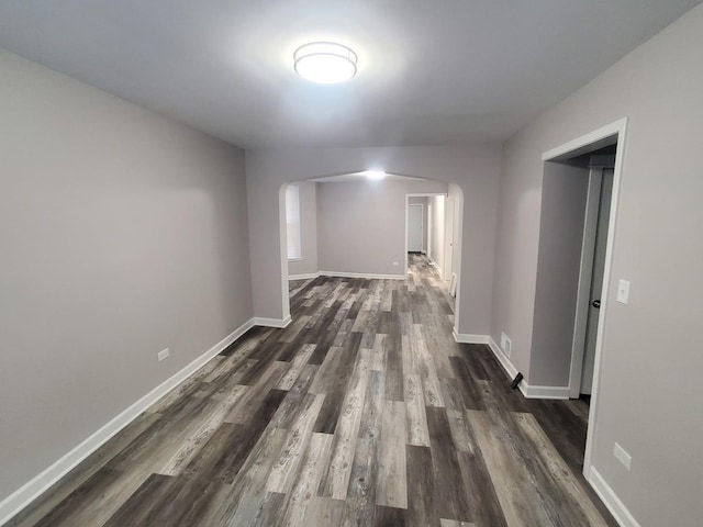 corridor with arched walkways, dark wood-style floors, and baseboards