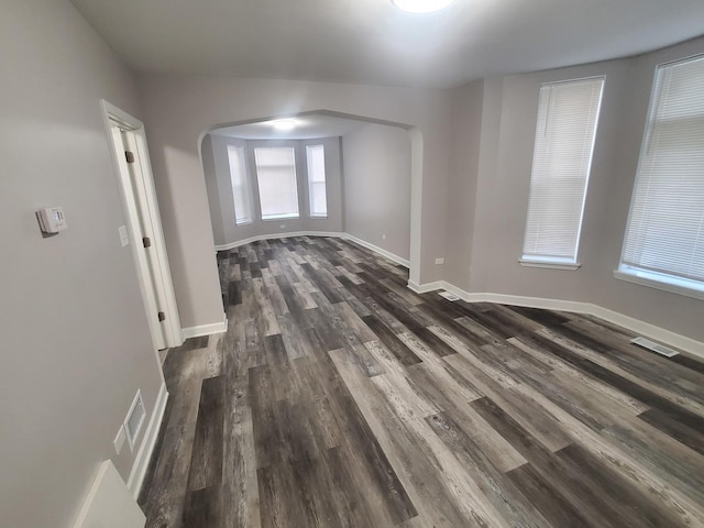 unfurnished room featuring dark wood-style floors, visible vents, arched walkways, and baseboards