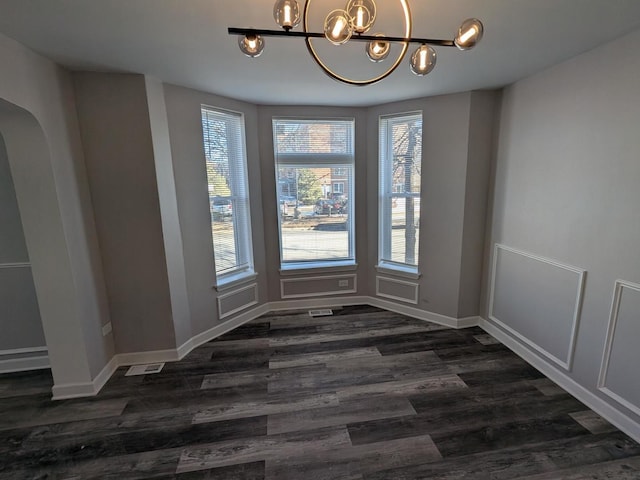 unfurnished dining area with baseboards, arched walkways, a notable chandelier, and wood finished floors