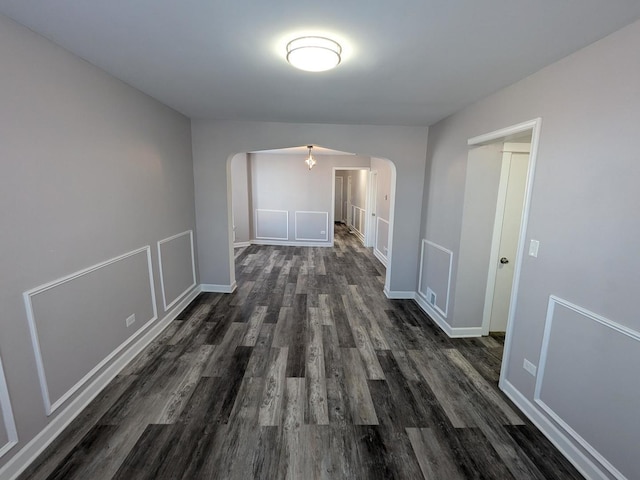 corridor with arched walkways, dark wood finished floors, and baseboards