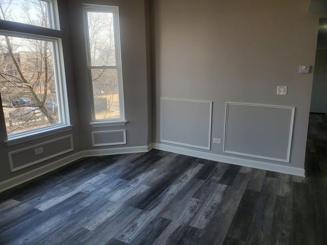 empty room featuring dark wood-type flooring, plenty of natural light, and baseboards