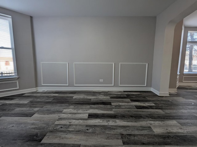 empty room featuring baseboards, arched walkways, and dark wood-style flooring