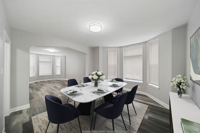 dining room with arched walkways, baseboards, and dark wood-style flooring