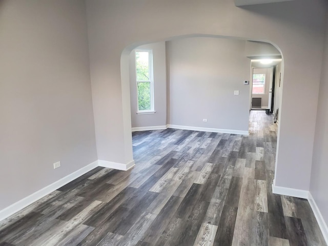 unfurnished room with arched walkways, a healthy amount of sunlight, and dark wood-style floors