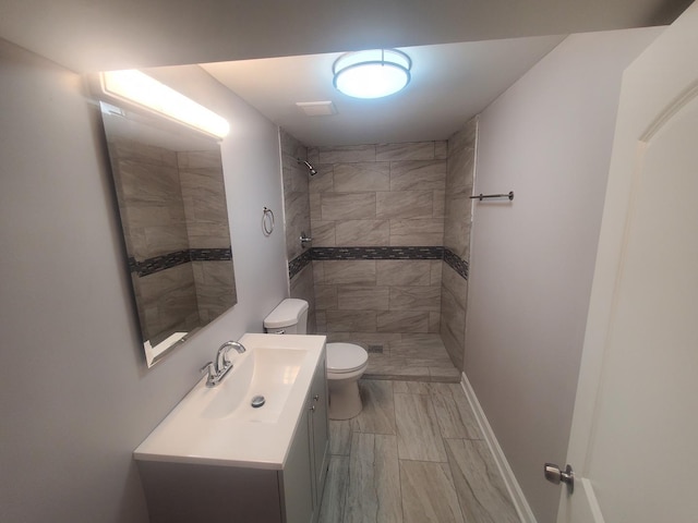 bathroom featuring a tile shower, vanity, and toilet