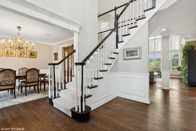 stairway with hardwood / wood-style floors, crown molding, a high ceiling, and an inviting chandelier