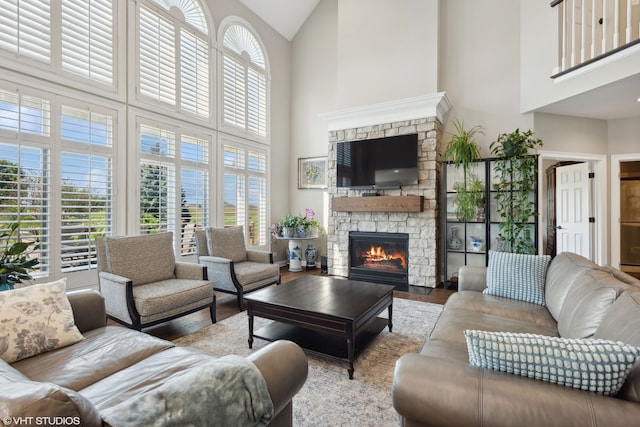 living room with a stone fireplace, hardwood / wood-style flooring, and a towering ceiling