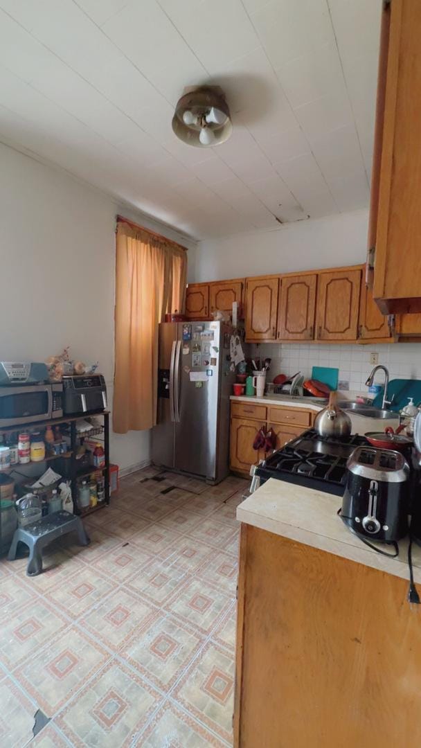 kitchen featuring decorative backsplash, light countertops, brown cabinets, a sink, and stainless steel refrigerator with ice dispenser