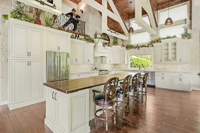 kitchen with high end refrigerator, beamed ceiling, stove, a kitchen island, and hardwood / wood-style flooring