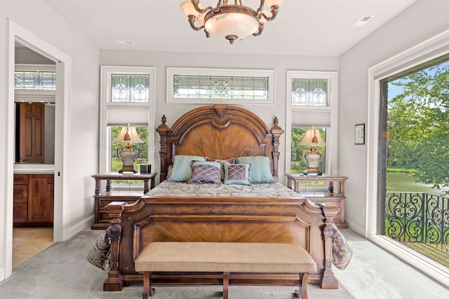 carpeted bedroom featuring a notable chandelier, ensuite bathroom, and multiple windows