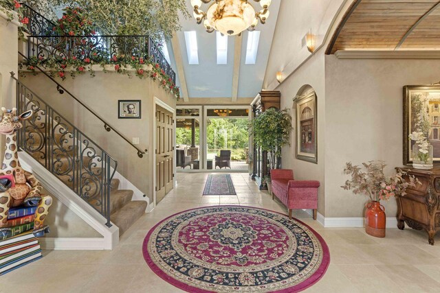 tiled entryway with high vaulted ceiling, an inviting chandelier, and wood ceiling