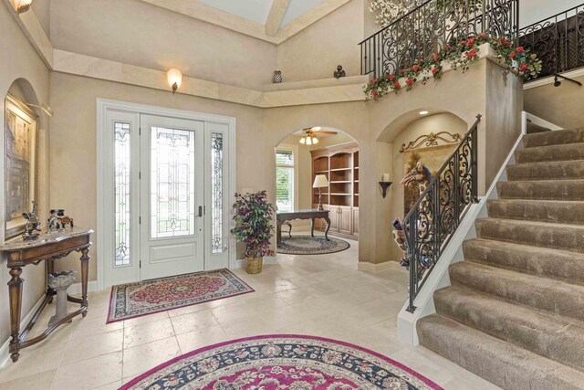 tiled entrance foyer with ceiling fan and a towering ceiling