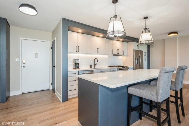 kitchen featuring a breakfast bar, decorative light fixtures, light wood-type flooring, decorative backsplash, and stainless steel appliances