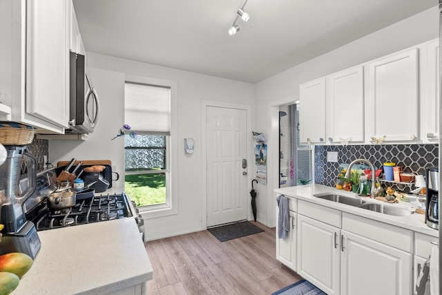 kitchen with backsplash, white cabinetry, rail lighting, sink, and light wood-type flooring