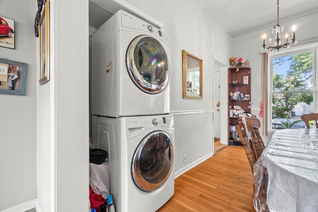 clothes washing area with stacked washer and dryer, light hardwood / wood-style flooring, and a chandelier